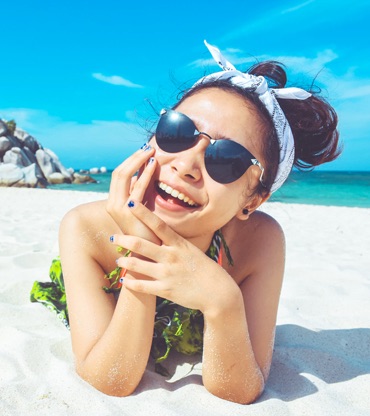 girl lying on white sand beach wearing sunglasses laughing