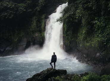 person looking away from camera at large waterfall in distance